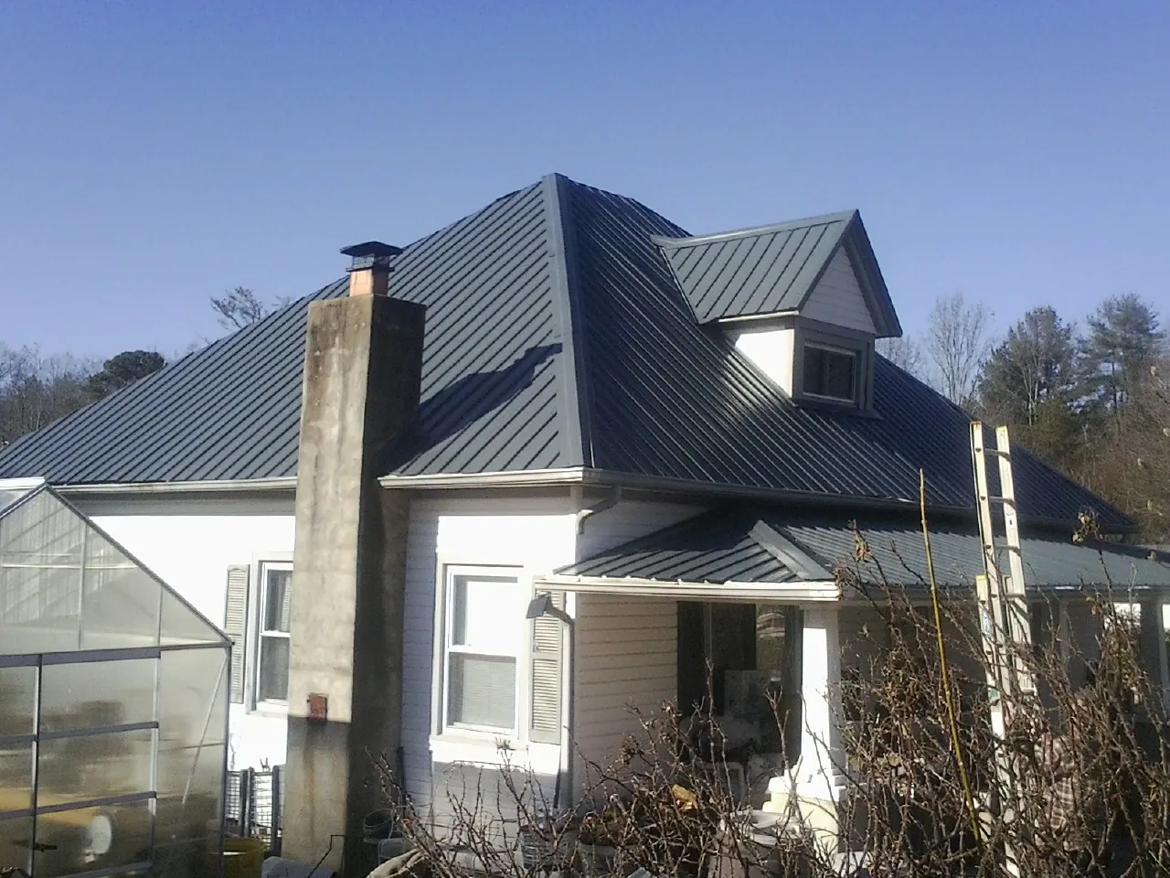 Dark blue standing seam metal roof on a white farmhouse with dormer — Slate & Tile Roof Repair by Roofing Brothers in Perley