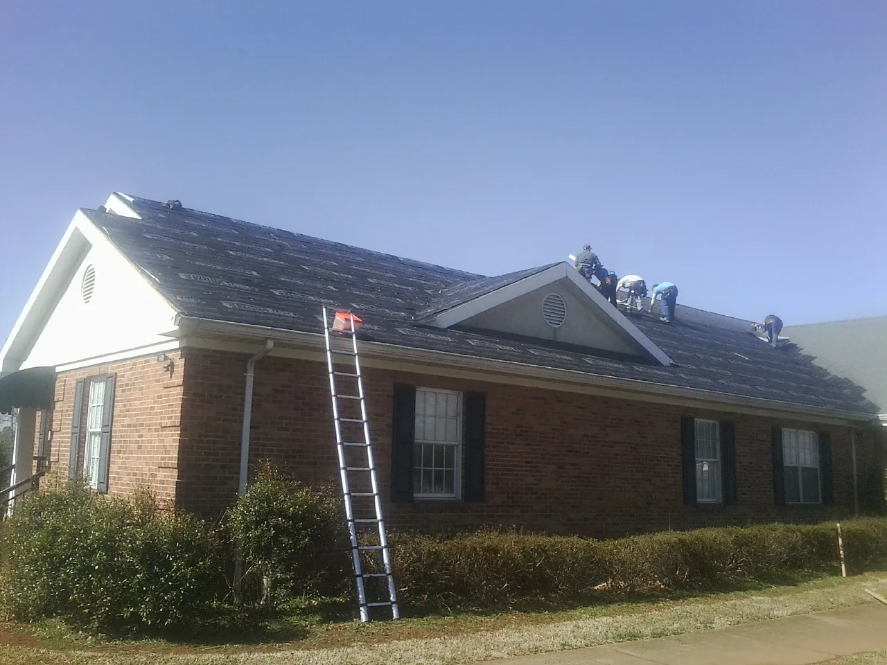 Crew tearing shingles off a brick ranch roof with a ladder set — Metal Roof Repair work by our crew in Perley