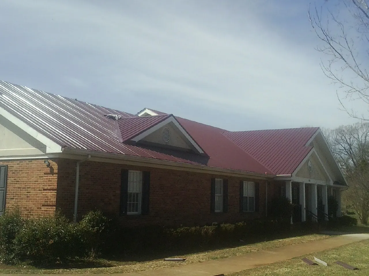 Red metal roof with gabled entries on a long brick building, from a Hail Damage Roof Repair job in Perley