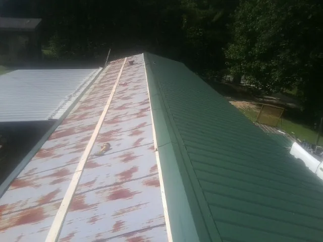 Old rusted panels beside newly installed green metal roofing — Wind Damage Roof Repair by Roofing Brothers in Perley