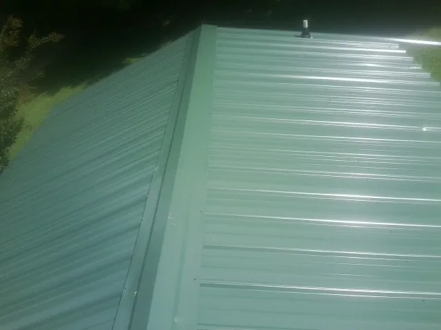 New green metal panels meeting at the ridge of a roof in Perley