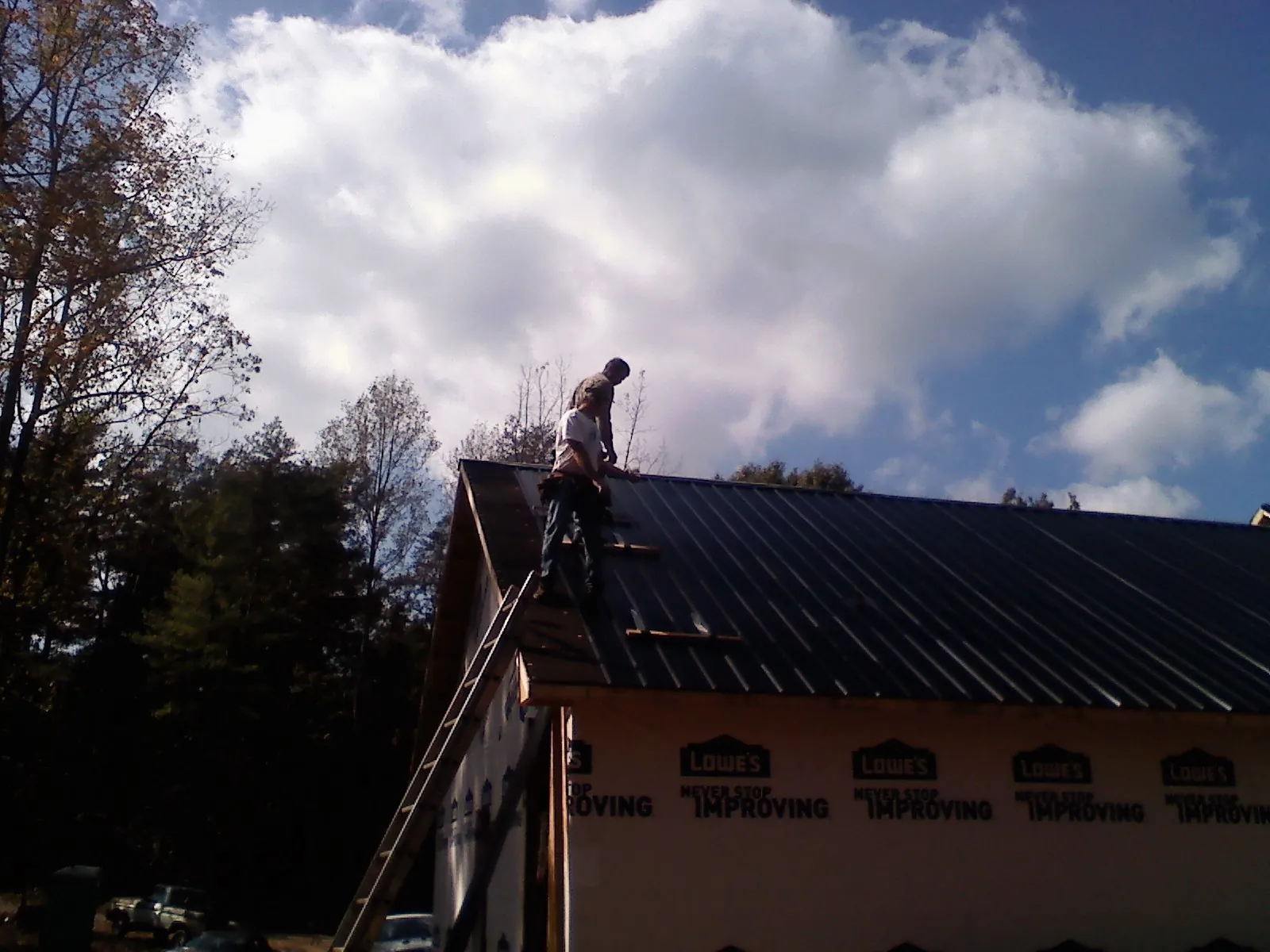 Roofer fastening dark metal panels high against a cloudy sky, from a Roof Inspection job in Perley
